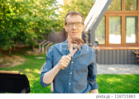 Middle-aged man holds a barbecue fork with slices of steak in his hand Middle-aged man holds a barbecue fork with slices of steak in his hand 116715863