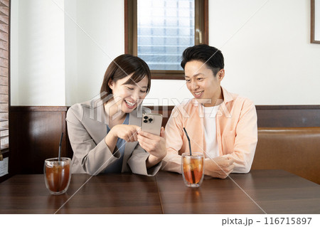 カフェでスマホの画面を見て会話するカップル 116715897