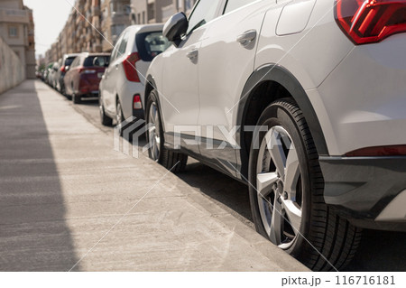 Row of diverse cars parked along urban street, illustrating the typical scene in city parking zone. Ideal for urban planning articles, parking management content, transportation theme illustrations. 116716181