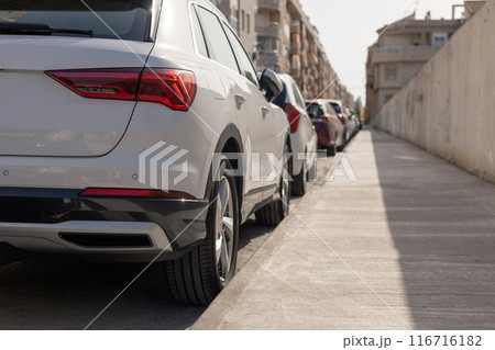 Row of cars parked along a sunny city street, showcasing urban parking dynamics. Ideal for articles on city transport, parking management solutions, and discussions on parking fees in urban settings. Row of cars parked along a sunny city street, showcasing urban parking dynamics. Ideal for articles on city transport, parking management solutions, and discussions on parking fees in urban settings. 116716182