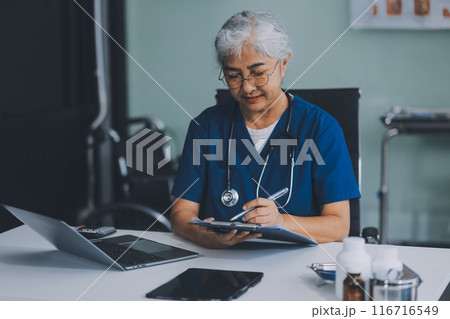 Thoughtful Hispanic female doctor sitting at her desk in a bright medical office, looking at a laptop screen. 116716549