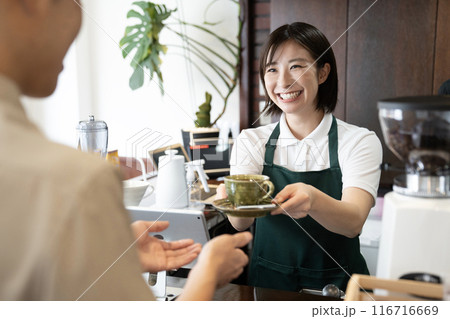 笑顔でコーヒーを渡すカフェの女性店員 116716669