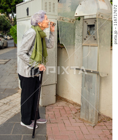 Time Stands Still: Senior Woman Inspects Abandoned Payphone, Reflects on the Pace of Progress 116717672