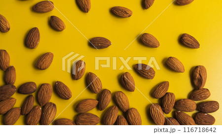 Vibrant close-up of scattered almonds on a bright yellow background 116718642