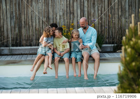 Cheerful family with three kids having fun together sitting by a pool. Cheerful family with three kids having fun together sitting by a pool. 116719906