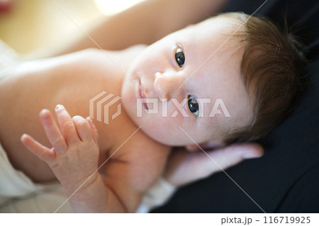 Portrait of cute little baby lying on bed, parents hands holding her. Portrait of cute little baby lying on bed, parents hands holding her. 116719925