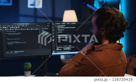 Happy self employed developer in home office doing coding on computer at desk. Joyful IT specialist doing contracted job from apartment, writing lines of code at workstation, camera A 116720419