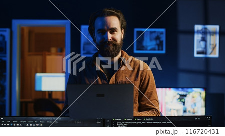 Portrait of smiling developer writing complex binary code scripts on laptop terminal. Cheerful remote IT employee standing in home office, using programming to safeguard consumer data, camera A 116720431