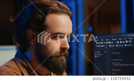 Software technician in apartment office deeply immersed in coding on computer at desk, close up. IT freelancer absorbed by work, focused on screen, writing lines of code at workstation, camera A 116720432