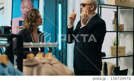 Skilled couturier asking for luxury items from store assistants, buying expensive clothing and materials for his new fashion show. Famous tailor is the patron or sponsor of the showroom. Camera A. Skilled couturier asking for luxury items from store assistants, buying expensive clothing and materials for his new fashion show. Famous tailor is the patron or sponsor of the showroom. Camera A. 116720478