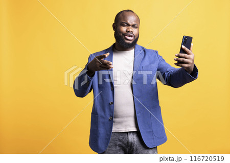 African american man excited to chat with friends during teleconference meeting using smartphone, studio background. Person having fun with mates during online video call on phone African american man excited to chat with friends during teleconference meeting using smartphone, studio background. Person having fun with mates during online video call on phone 116720519