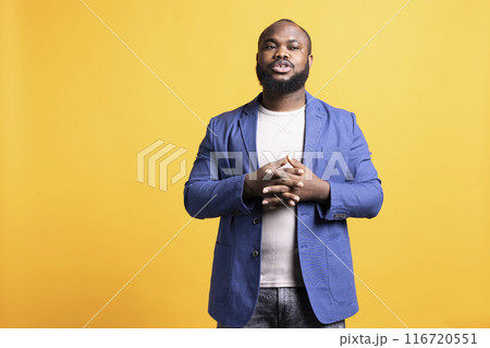 Uneasy african american man posing and holding hands together, isolated over yellow studio background. BIPOC person feeling anxious, waiting for something, looking to the side 116720551