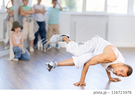 Young male coach demonstrating to group of teen children hip hop dance moves in class 116723976