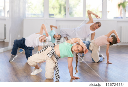 Dynamic young girl sitting in breakdance pose in dance studio with other teenage dancers Dynamic young girl sitting in breakdance pose in dance studio with other teenage dancers 116724384