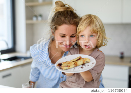 Mom and son eating pancakes together, morning in the kitchen for singel mother. Parents and children spending weekend day indoors. 116730054