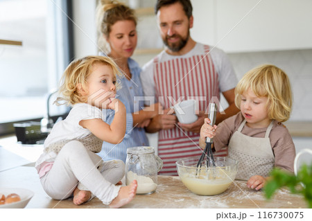 Young nuclear family making pancakes together. Parents and children in kitchen, preparing pancake batter, spending weekend day indoors. Young nuclear family making pancakes together. Parents and children in kitchen, preparing pancake batter, spending weekend day indoors. 116730075