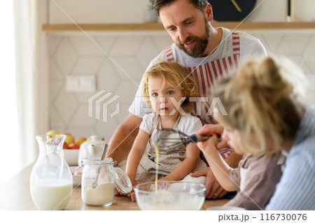 Young nuclear family making pancakes together. Parents and children in kitchen, preparing pancake batter, spending weekend day indoors. Young nuclear family making pancakes together. Parents and children in kitchen, preparing pancake batter, spending weekend day indoors. 116730076