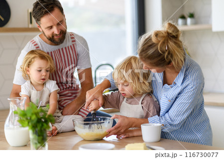 Young nuclear family making pancakes together. Parents and children in kitchen, preparing pancake batter, spending weekend day indoors. Young nuclear family making pancakes together. Parents and children in kitchen, preparing pancake batter, spending weekend day indoors. 116730077