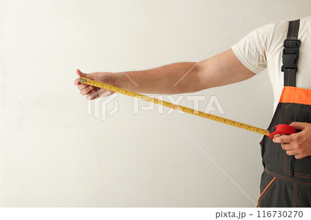 Hand holding tape measure profile. Construction worker measuring wall with tape measure, white background 116730270