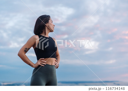 A woman in sportswear looks confidently during sunset, displaying strength and determination A woman in sportswear looks confidently during sunset, displaying strength and determination 116734148