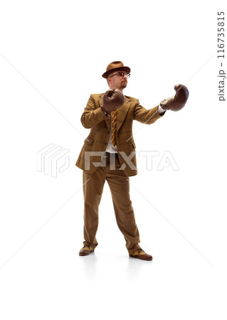 Man in formal outfit stands in boxing stance wearing boxing gloves, focused and ready to spar against white studio background. 116735815