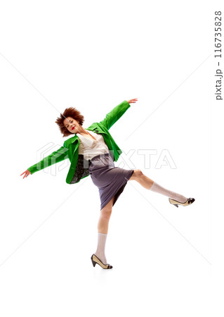 Young woman, dressed vivid vintage outfit dancing in motion exuding confidence and energy against white studio background. 116735828