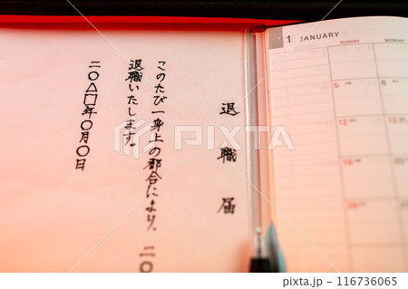 手書きで書かれた退職届の文面と新しいスケジュール帳とペンの先端部分をを赤系のライトで。 116736065