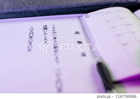 手書きで書かれた退職届の文面と新しいスケジュール帳とペンの先端部分をを青系のライトで。 116736066