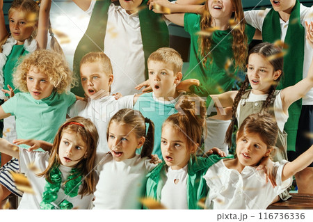 Children dressed in green and white cheering enthusiastically and hugs and golden confetti falling around them. Children dressed in green and white cheering enthusiastically and hugs and golden confetti falling around them. 116736336