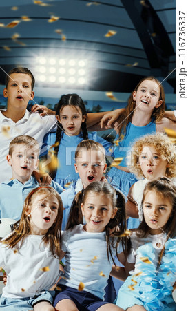 Children dressed in blue and white are huddled together, cheering and singing with joy supporting their favorite soccer team. Children dressed in blue and white are huddled together, cheering and singing with joy supporting their favorite soccer team. 116736337