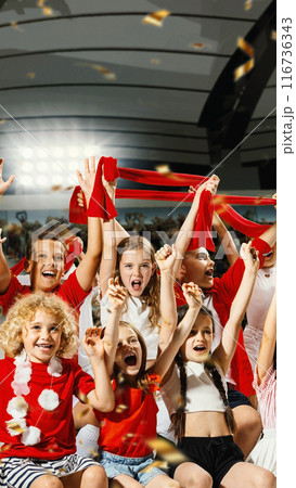 Jubilant children, dressed in red and white, enthusiastically wave red scarves and cheer with confetti flying around. Celebratory mood. 116736343