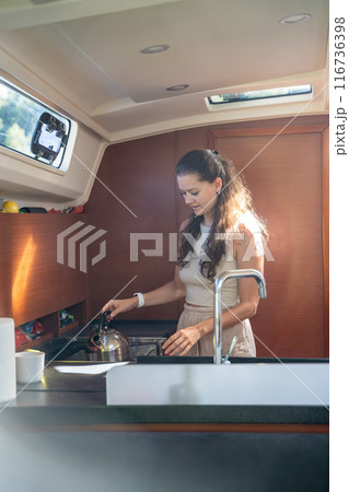 Young woman standing and preparing tea in kitchen in cabin of modern yacht during sailing in sea. Yacht life concept Young woman standing and preparing tea in kitchen in cabin of modern yacht during sailing in sea. Yacht life concept 116736398