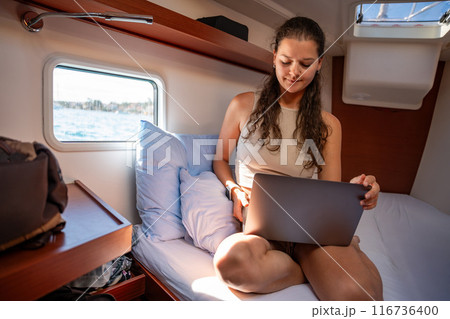 Young woman freelancer using laptop near window in the cabin of a yacht during sailing in sea. Yacht life concept 116736400