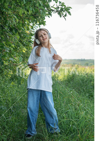 A child  with headphones listening to music and dancing in the park.. 116736458