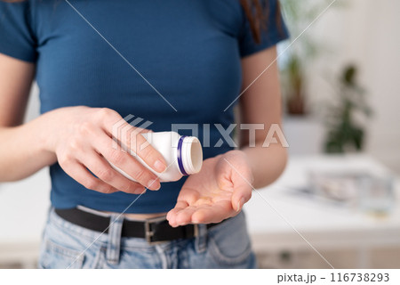 Young woman holds capsules in a hand, female takes supplements and vitamins from a bottle, close-up view. 116738293
