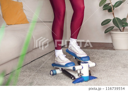 A sports girl in leggings works at home on a stepper. Home fitness. Woman following figure. Close up cropped 116739554