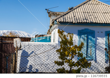 Rustic house with corrugated slate roof in small town and blue windows stands under a clear sky with snowcapped mountain range on the horizon 116739555