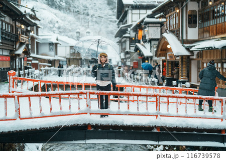 Woman tourist Visiting Ginzan Onsen in Yamagata, happy Traveler sightseeing Japanese Onsen village with Snow in winter season. landmark and popular for attraction in Japan. Travel and Vacation concept 116739578