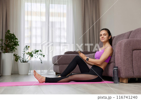 sporty woman sitting with smartphone and looking at the camera at home 116741240