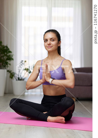 Caucasian woman practicing yoga and meditation sitting in lotus pose on pink yoga mat at home 116741270