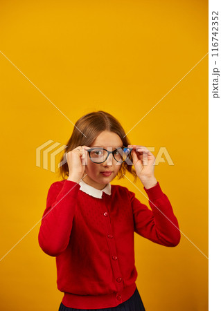 Teenage Girl in School Uniform Holding Glasses Against a Bright Yellow Background Teenage Girl in School Uniform Holding Glasses Against a Bright Yellow Background 116742352