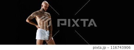 Handsome young bald man posing in white underwear, showing perfect muscular tattooed body against black studio background Handsome young bald man posing in white underwear, showing perfect muscular tattooed body against black studio background 116743906