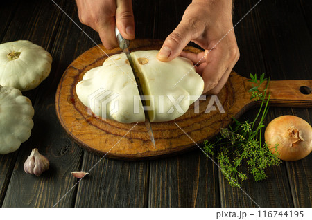 A knife in a man hands slicing zucchini on a wooden kitchen board before preparing a tasty and healthy dinner at home 116744195