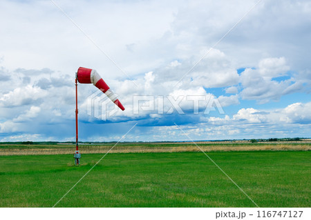 Weather vane in the airfield with grass and dramatic cloudy sky. 116747127