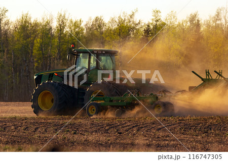 John Deere tractor and seeder working in the field in sunset. 116747305