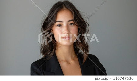 Young Woman Wearing Black Blazer and Necklace Against a Gray Wall 116747536