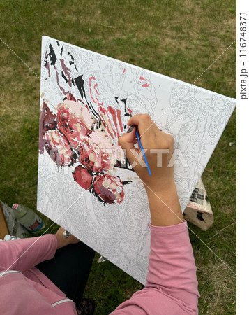 The woman writes a picture by numbers. Paints in numbered jars and a can of water. On open air. Close-up. 116748371