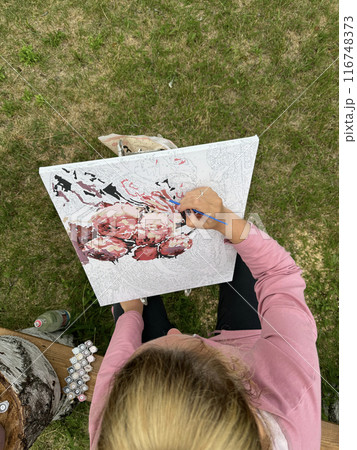 The woman writes a picture by numbers. Paints in numbered jars and a can of water. On open air. Filmed from above. The woman writes a picture by numbers. Paints in numbered jars and a can of water. On open air. Filmed from above. 116748373