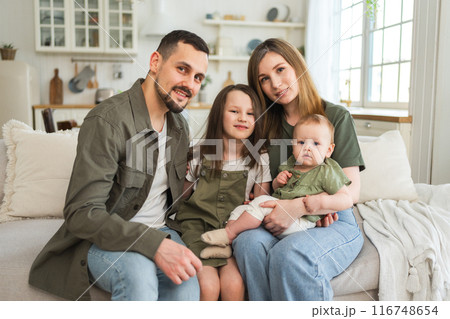 Happy family at home. Mother father two children daughters relaxing on sofa indoor. Mom dad parents baby girls kids relax playing having fun together. Family smiling laughing enjoying tender moment Happy family at home. Mother father two children daughters relaxing on sofa indoor. Mom dad parents baby girls kids relax playing having fun together. Family smiling laughing enjoying tender moment 116748654