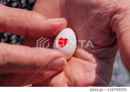 Womans hands holding a small egg with red heart symbol. Womans hands holding a small egg with red heart symbol. 116749505